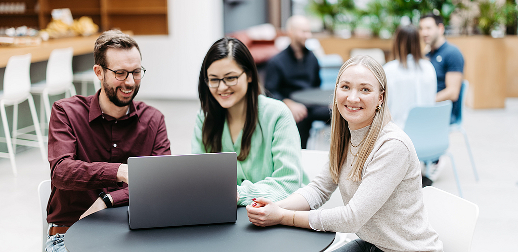 Drei Kolleg:innen sitzen am Tisch vor einem Laptop