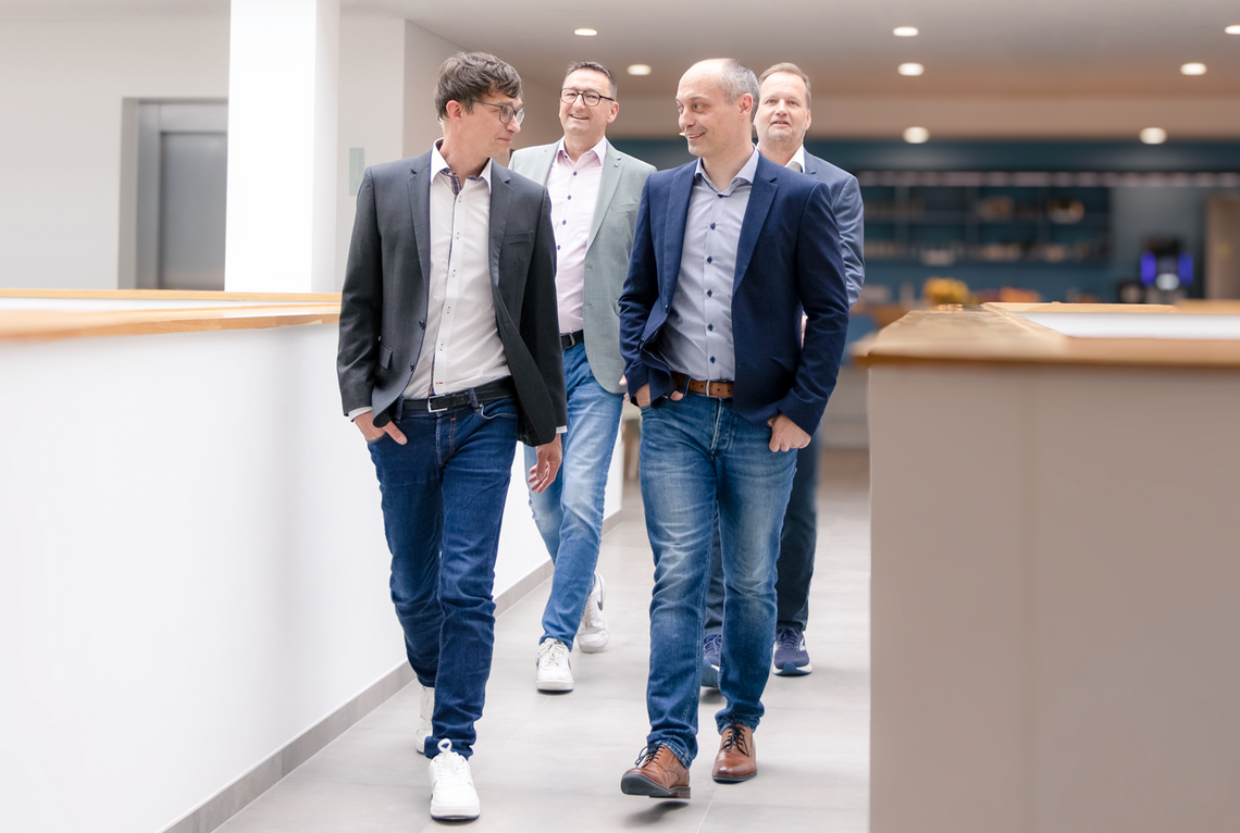 Four men walk together through a modern office.