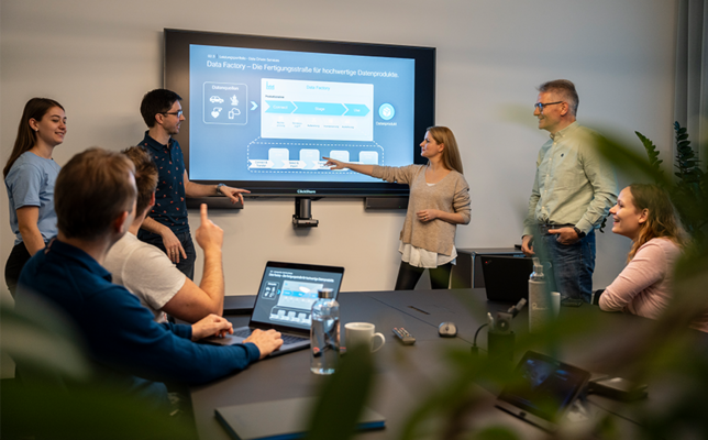People who are in a meeting, a woman points at a screen with a graphic