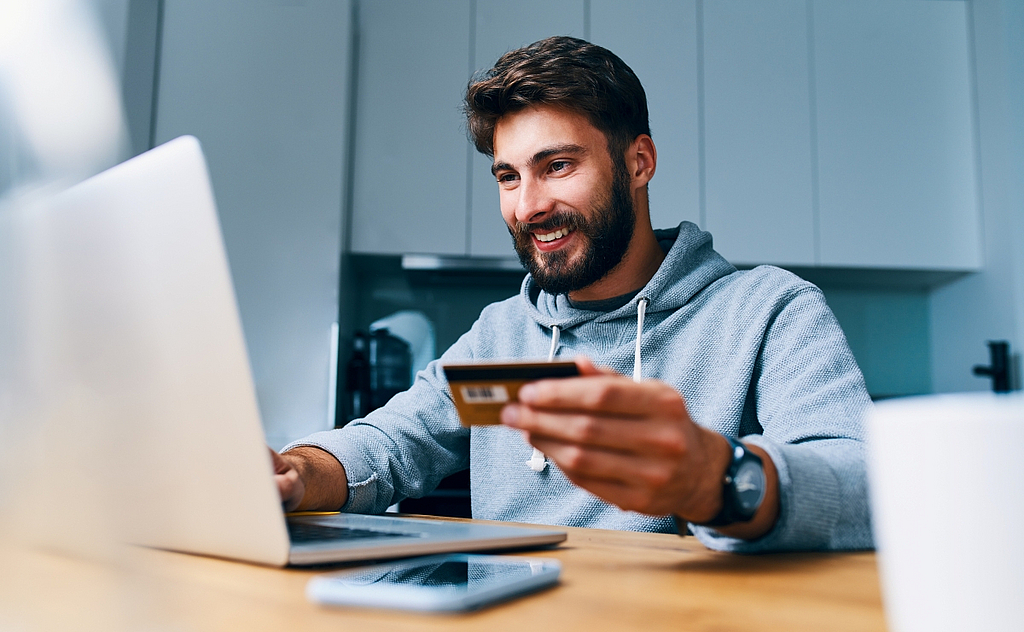 Mann vor Laptop mit Kreditkarte in der Hand am Zahlungsvorgang online