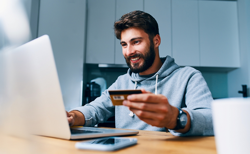 Mann vor Laptop mit Kreditkarte in der Hand am Zahlungsvorgang online