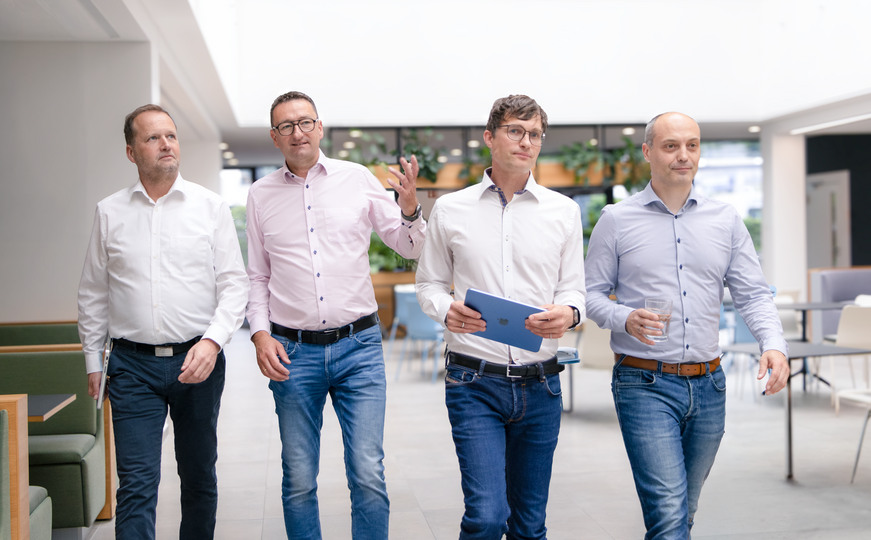 Vier Männer gehen gemeinsam durch ein modernes Büro.