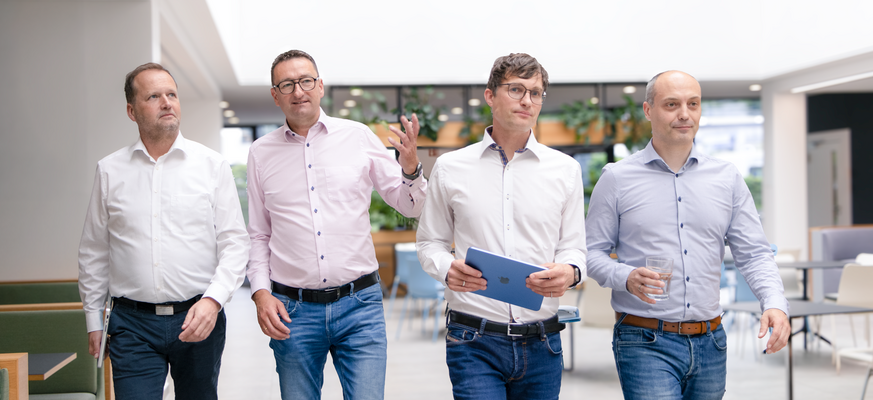 Vier Männer gehen gemeinsam durch ein modernes Büro.