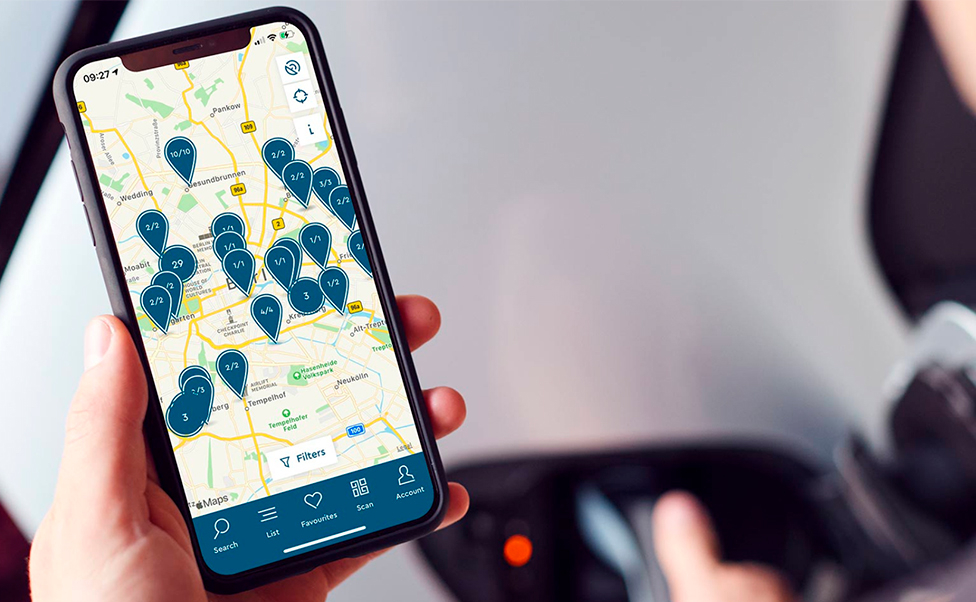 Mann schaut auf Smartphone auf dem eine digitale Karte zur Verfügbarkeit von E-Lade Stationen offen ist