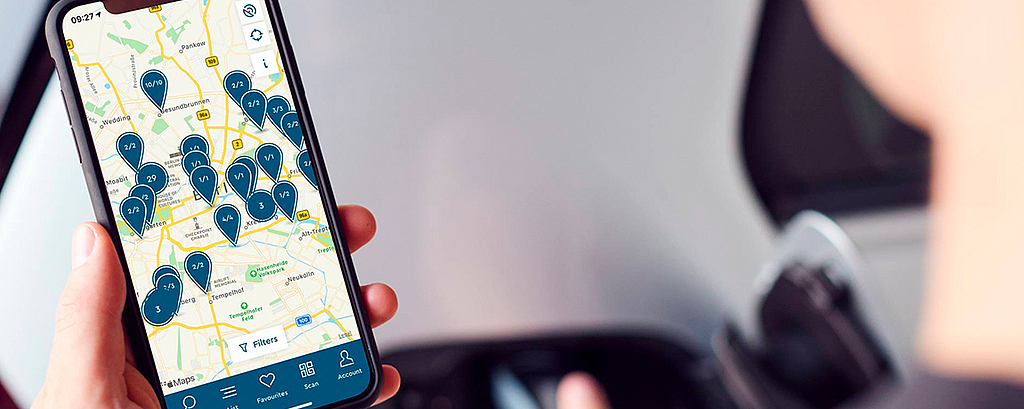 Mann schaut auf Smartphone auf dem eine digitale Karte zur Verfügbarkeit von E-Lade Stationen offen ist