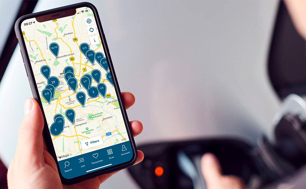 Mann schaut auf Smartphone auf dem eine digitale Karte zur Verfügbarkeit von E-Lade Stationen offen ist