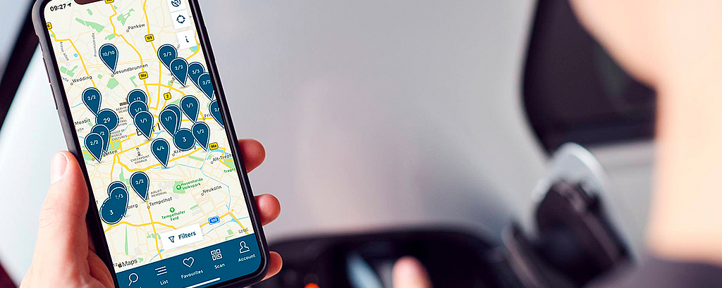 Mann schaut auf Smartphone auf dem eine digitale Karte zur Verfügbarkeit von E-Lade Stationen offen ist