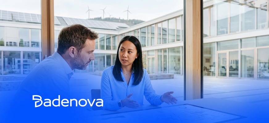 Zwei Personen im Gespräch; modernes Gebäude mit Solaranlagen und Windrädern im Hintergrund. „Badenova“-Logo unten links. – KI-generiertes Bild