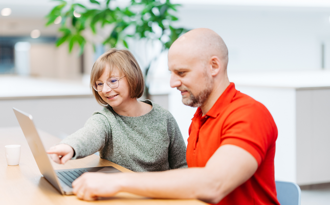 A woman and a man are looking at a laptop together. The woman points at the laptop.