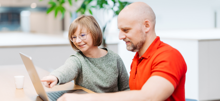 Eine Frau und ein Mann schauen gemeinsam auf einen Laptop. Die Frau zeigt auf den Laptop.