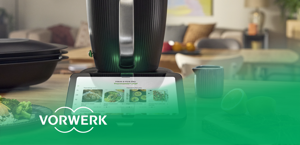 Thermomix mit Display zur Rezeptauswahl auf einer Küchenarbeitsfläche. „Vorwerk“-Logo unten links.