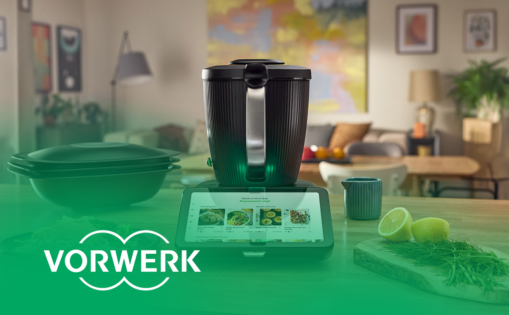Thermomix with a display for recipe selection on a kitchen countertop. “Vorwerk” logo bottom left.