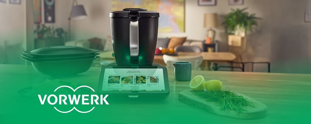 Thermomix with a display for recipe selection on a kitchen countertop. “Vorwerk” logo bottom left.
