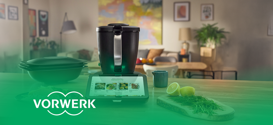 Thermomix mit Display zur Rezeptauswahl auf einer Küchenarbeitsfläche. „Vorwerk“-Logo unten links.