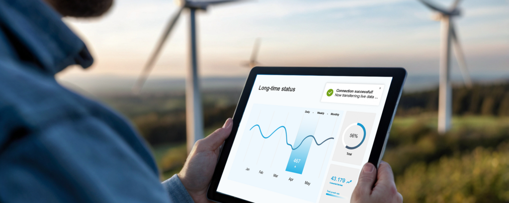 Person hält ein Tablet mit IoT-Dashboard vor Windrädern; angezeigt wird ein Statusdiagramm mit Live-Daten und Verbindungsinfo.