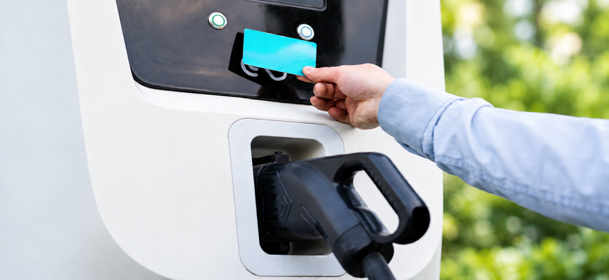 Eine Person hält eine Ladekarte an das Lesegerät einer E-Auto-Ladesäule mit eingestecktem Ladestecker.
