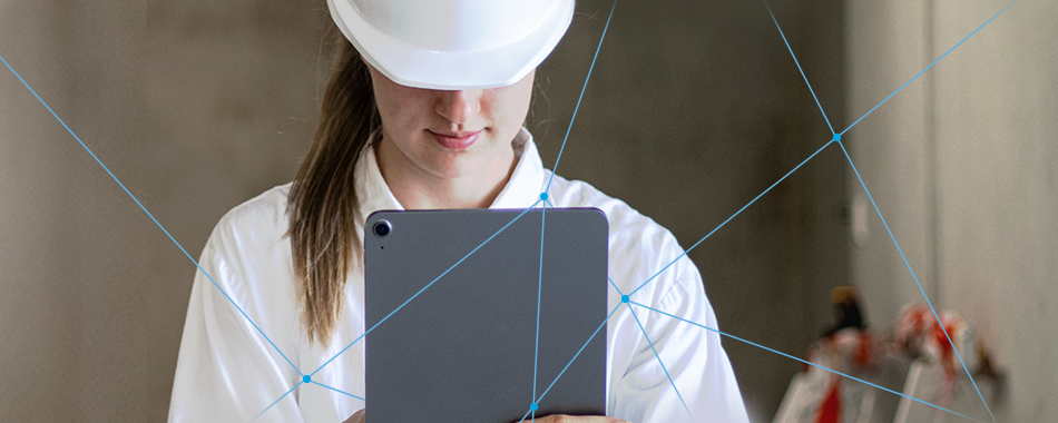 Junge Frau mit weißem Schutzhelm und Laborkittel schaut auf ein Tablet