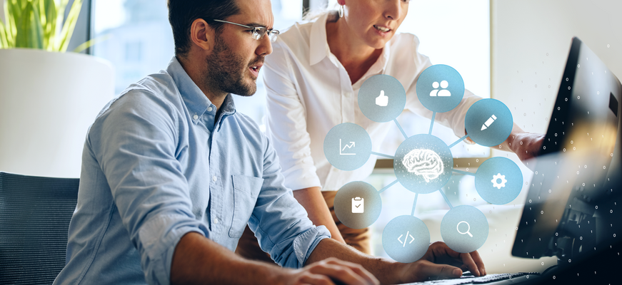 Zwei Personen arbeiten gemeinsam am Computer; darüber eine Grafik mit vernetztem Gehirn-Symbol und Icons für Daten, Analyse und digitale Prozesse.