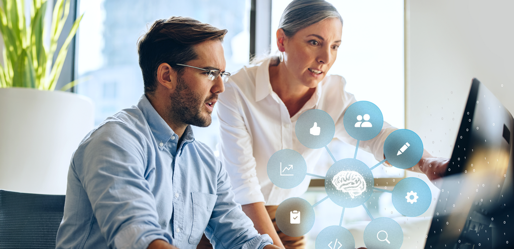 Zwei Personen arbeiten gemeinsam am Computer; darüber eine Grafik mit vernetztem Gehirn-Symbol und Icons für Daten, Analyse und digitale Prozesse.