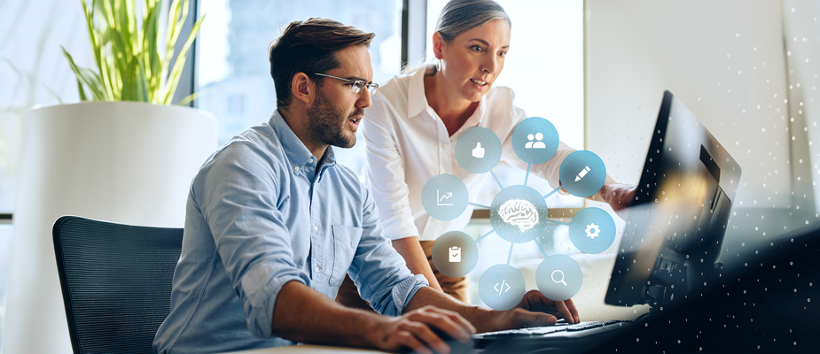 Two people are working together at a computer, with a graphic above them showing a connected brain symbol and icons for data, analytics, and digital processes.