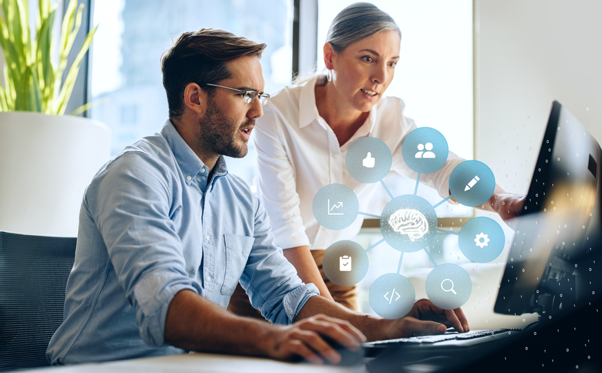Zwei Personen arbeiten gemeinsam am Computer; darüber eine Grafik mit vernetztem Gehirn-Symbol und Icons für Daten, Analyse und digitale Prozesse.