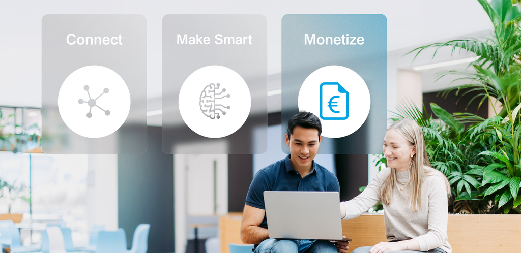 Two employees with laptops in a bright office environment; above them, the four service areas “Individual Solutions,” “Connect,” “Make Smart,” and ‘Monetize’ are displayed as visual navigation tiles. “Monetize” is highlighted.
