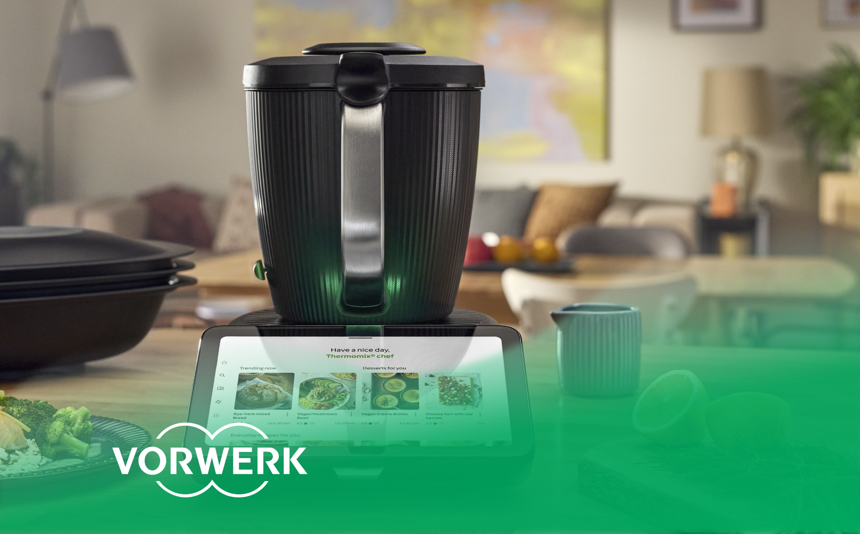 Thermomix with a display for recipe selection on a kitchen countertop. “Vorwerk” logo bottom left.