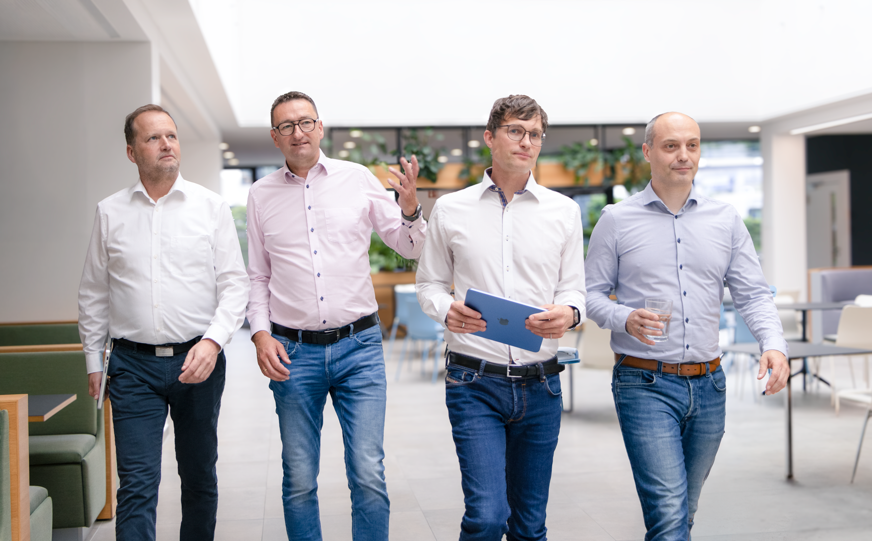 Four men walk together through a modern office.